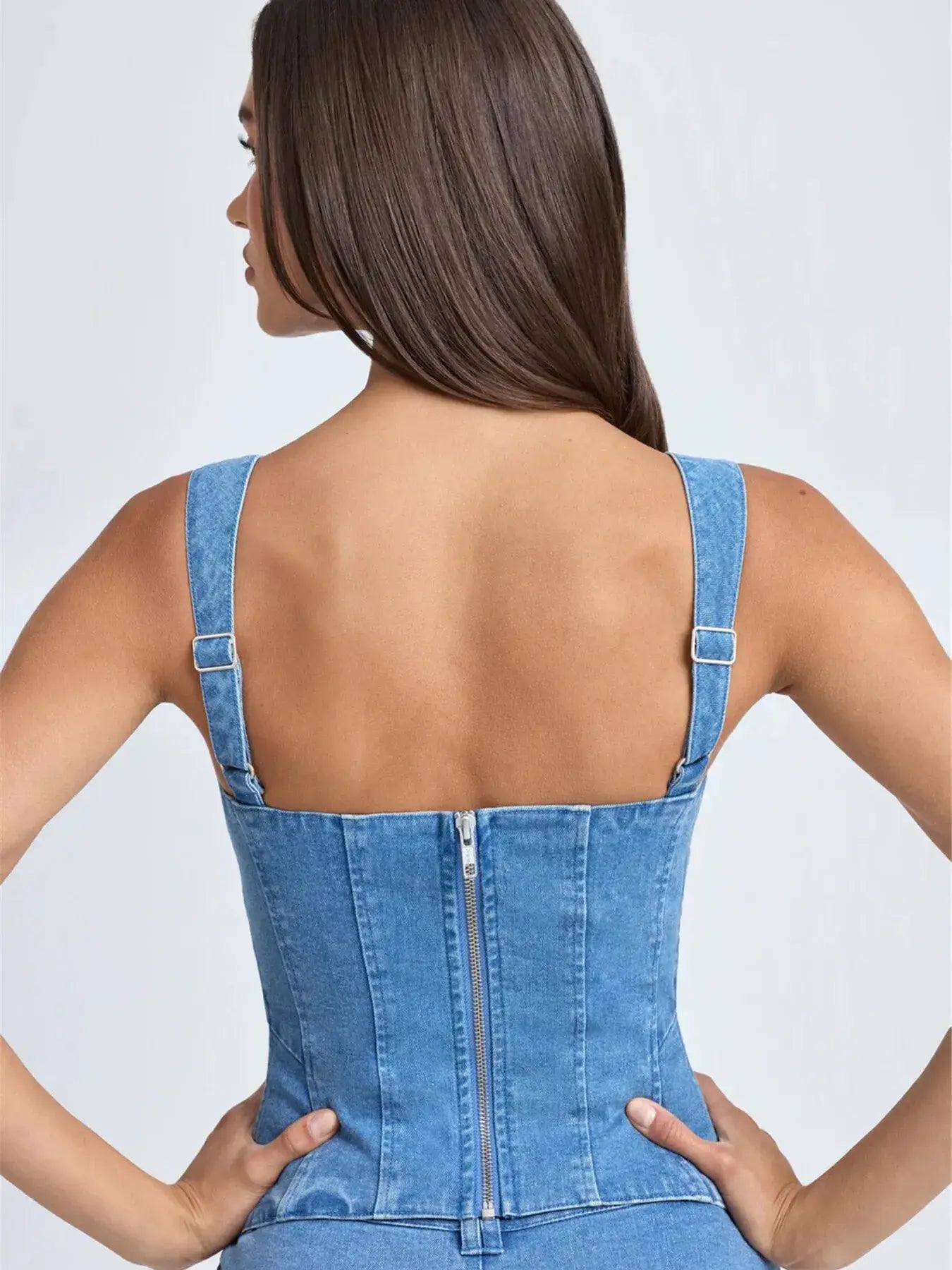 Woman wearing a blue denim corset back view with a plain background