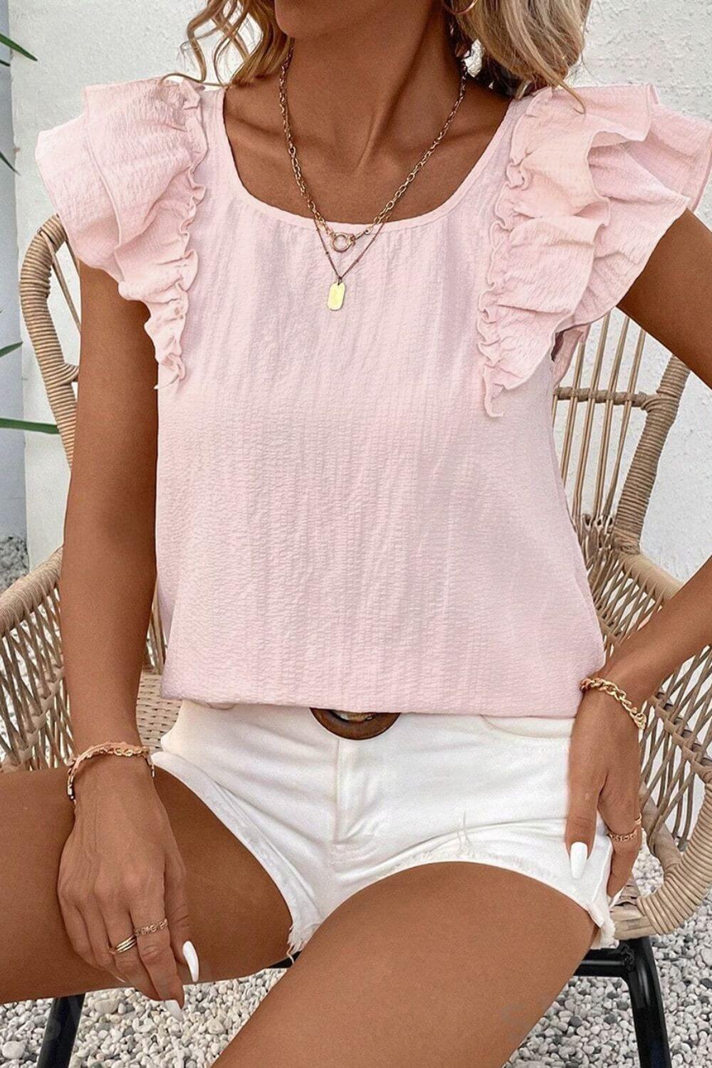 Woman wearing a pink ruffled top and white shorts sitting on a wicker chair.