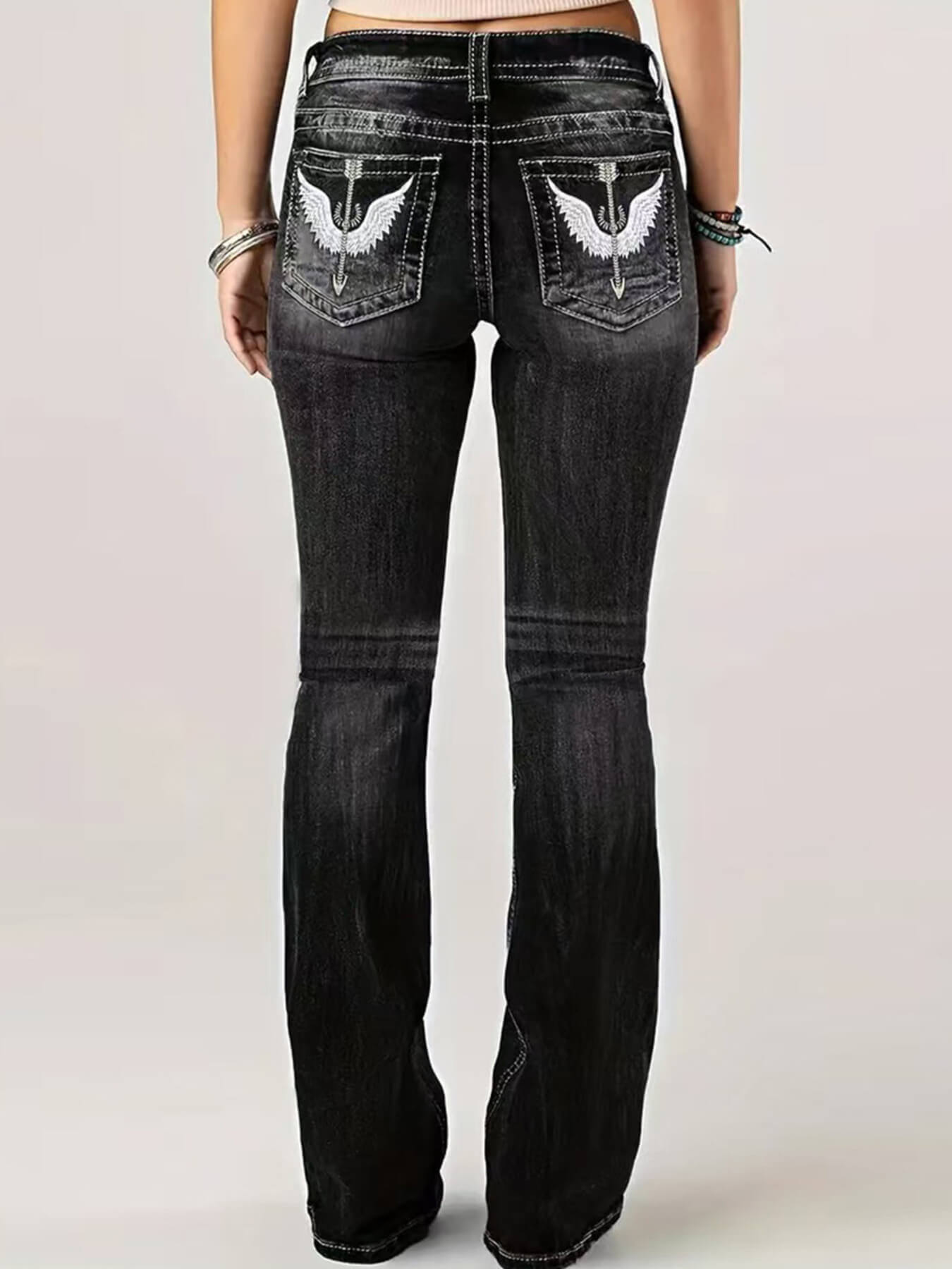 Black jeans with angel wing designs on the pockets against a light background